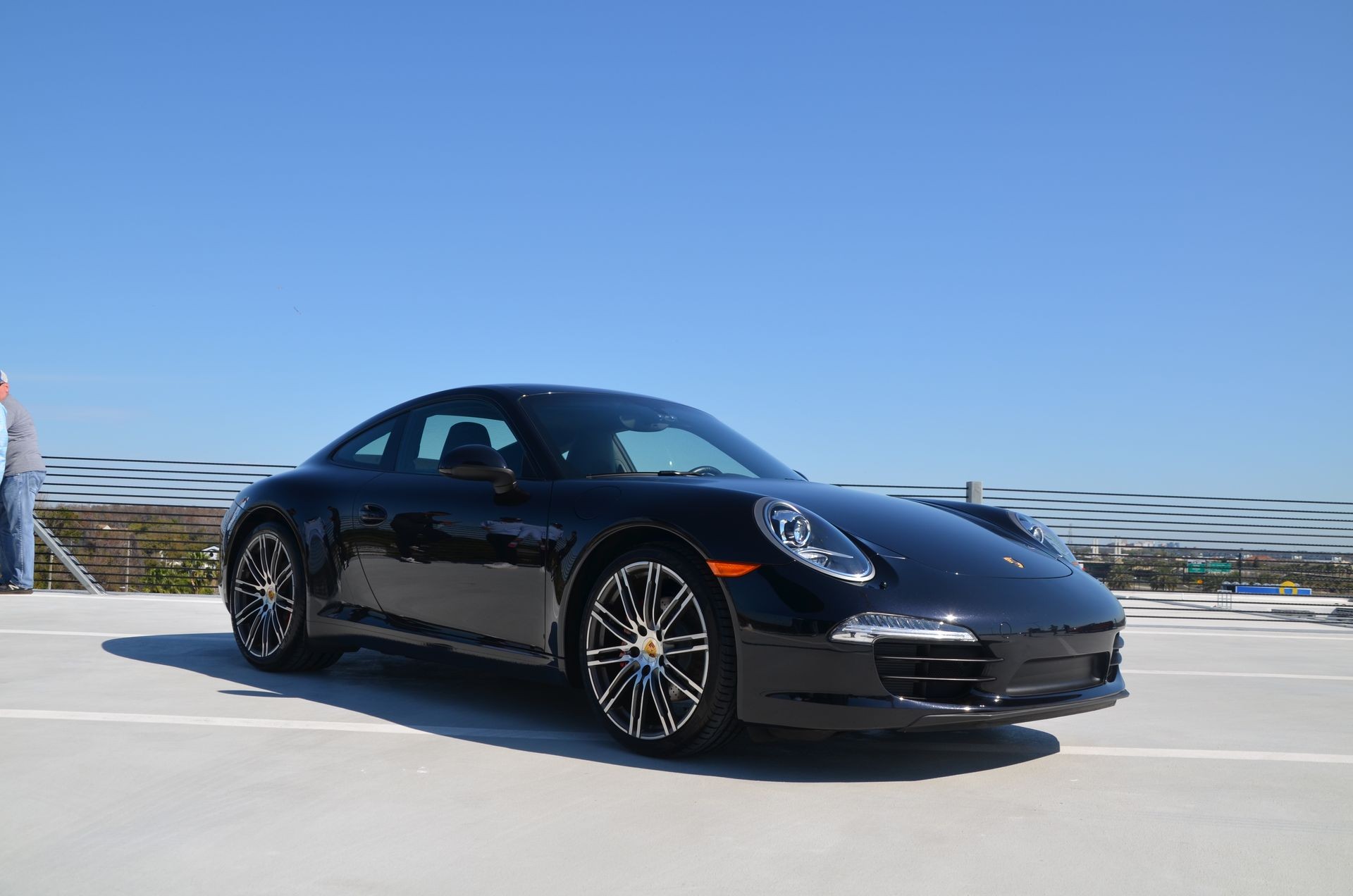 Sleek black sports car parked on a rooftop with a clear blue sky in the background.