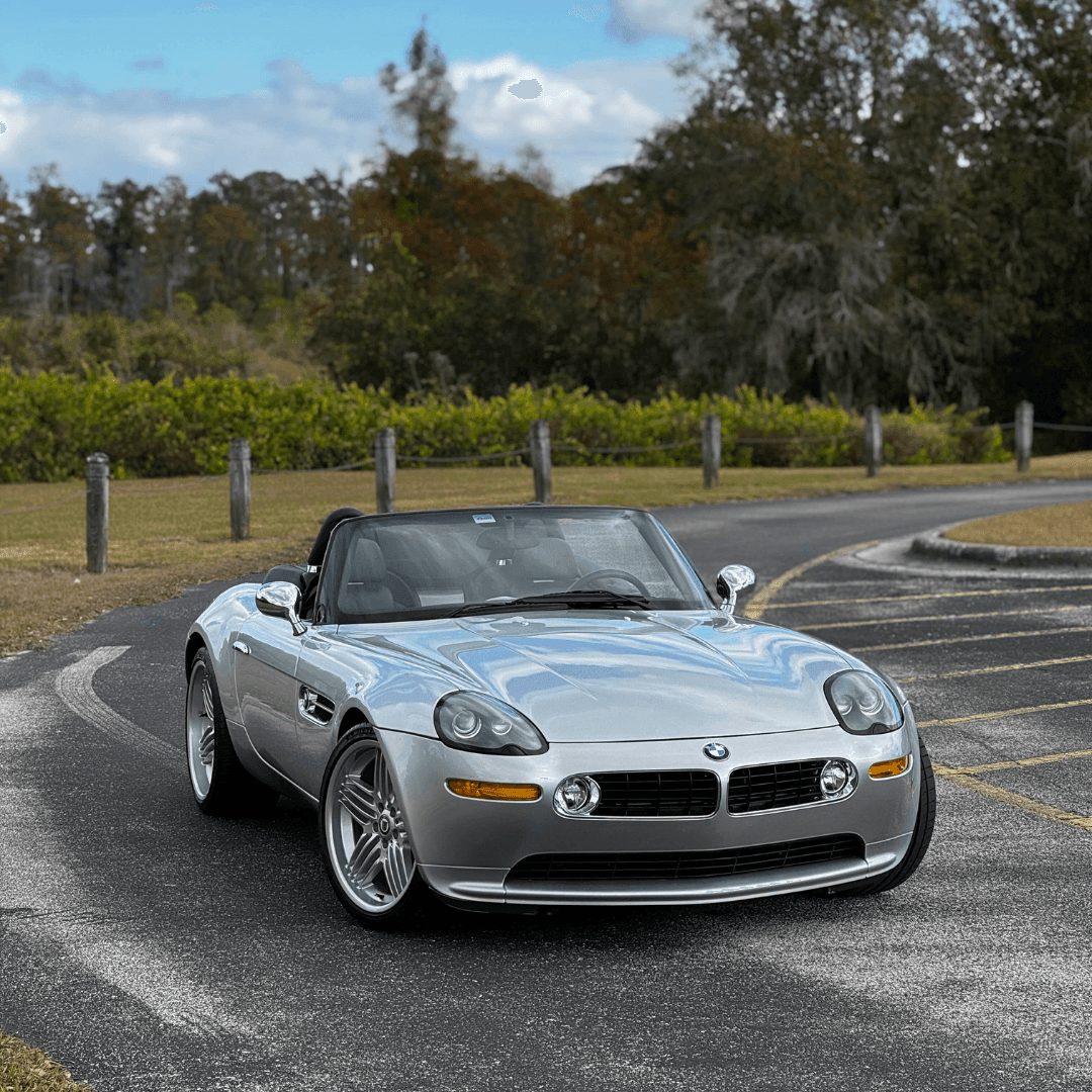 Silver convertible sports car on a scenic road with trees in the background.