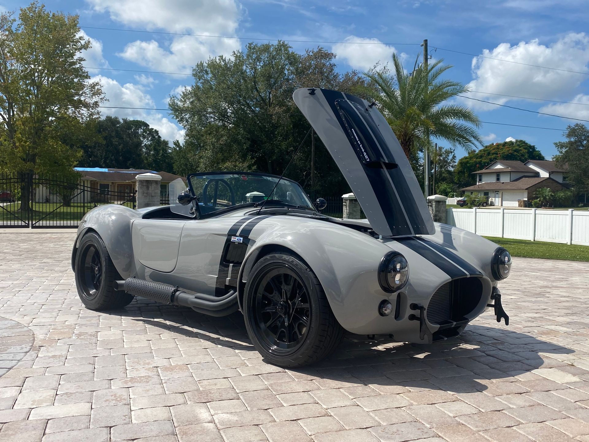 Gray vintage convertible sports car with open hood on a sunny day in a residential area.