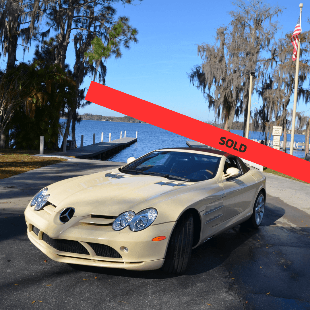 Luxury beige sports car parked by a lake with a red 'SOLD' banner overlay.