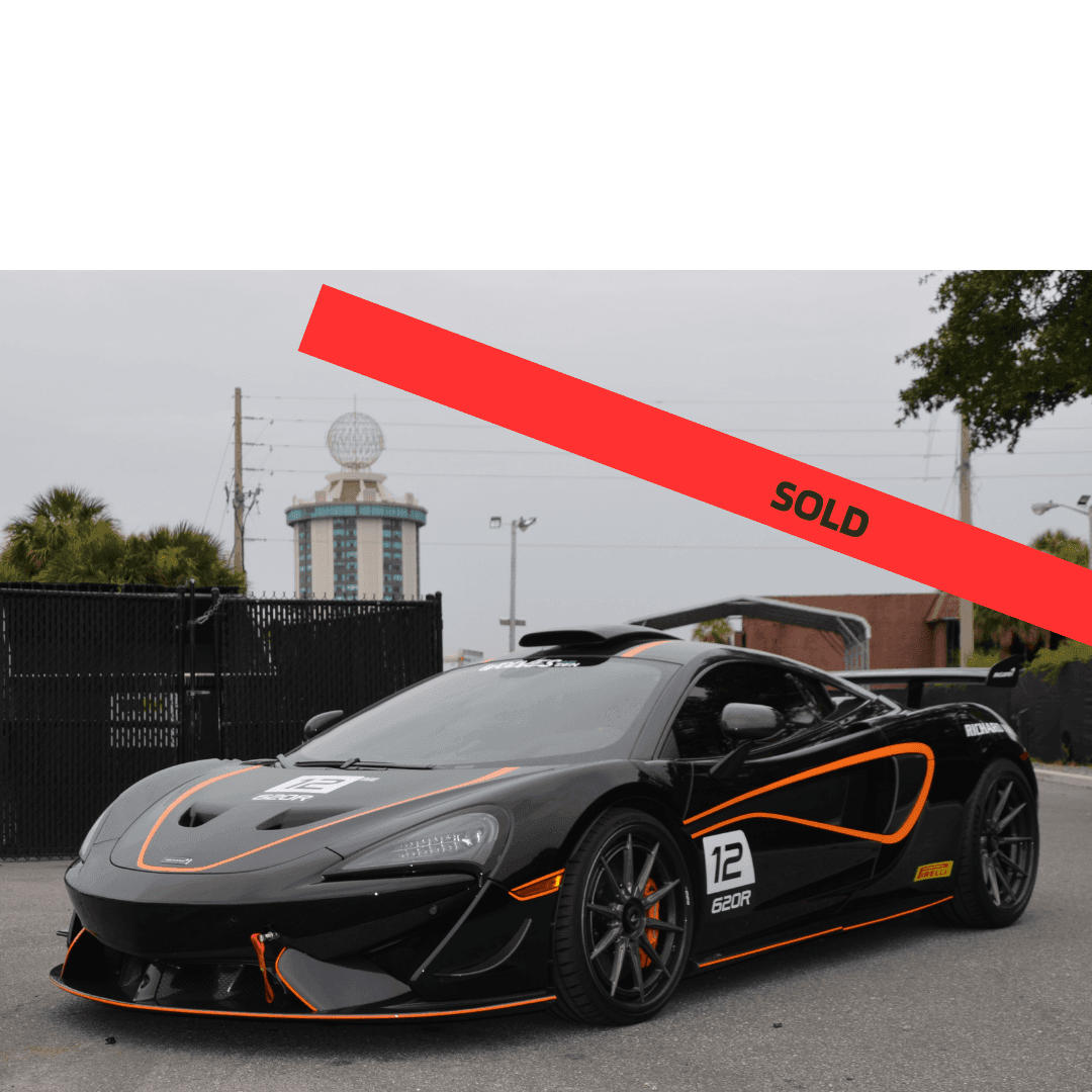 Black sports car with orange accents and 'SOLD' banner across the image, parked outdoors.